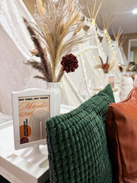 Cozy boho indoor sleepover setup with miniature teepees, white trays, textured green and rust pillows, dried pampas grass centerpiece, fairy lights and a framed birthday sleepover sign