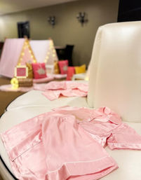 Pink satin pajamas draped on white seating in front of mini pink teepees with fairy lights and colorful pillows — indoor kids' slumber party setup
