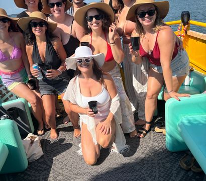 Smiling group in wide-brim hats and sunglasses enjoying a sunny summer boat party on a yellow pontoon over calm coastal waters