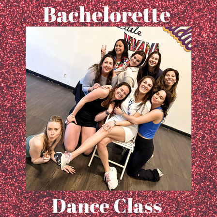 Bachelorette dance class — a group of women laughing and posing in a dance studio around the bride-to-be seated on a folding chair, hardwood floor and colorful wall art in the background.