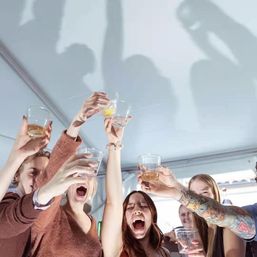 Group of friends cheering and raising plastic cups for a celebratory toast inside a party tent