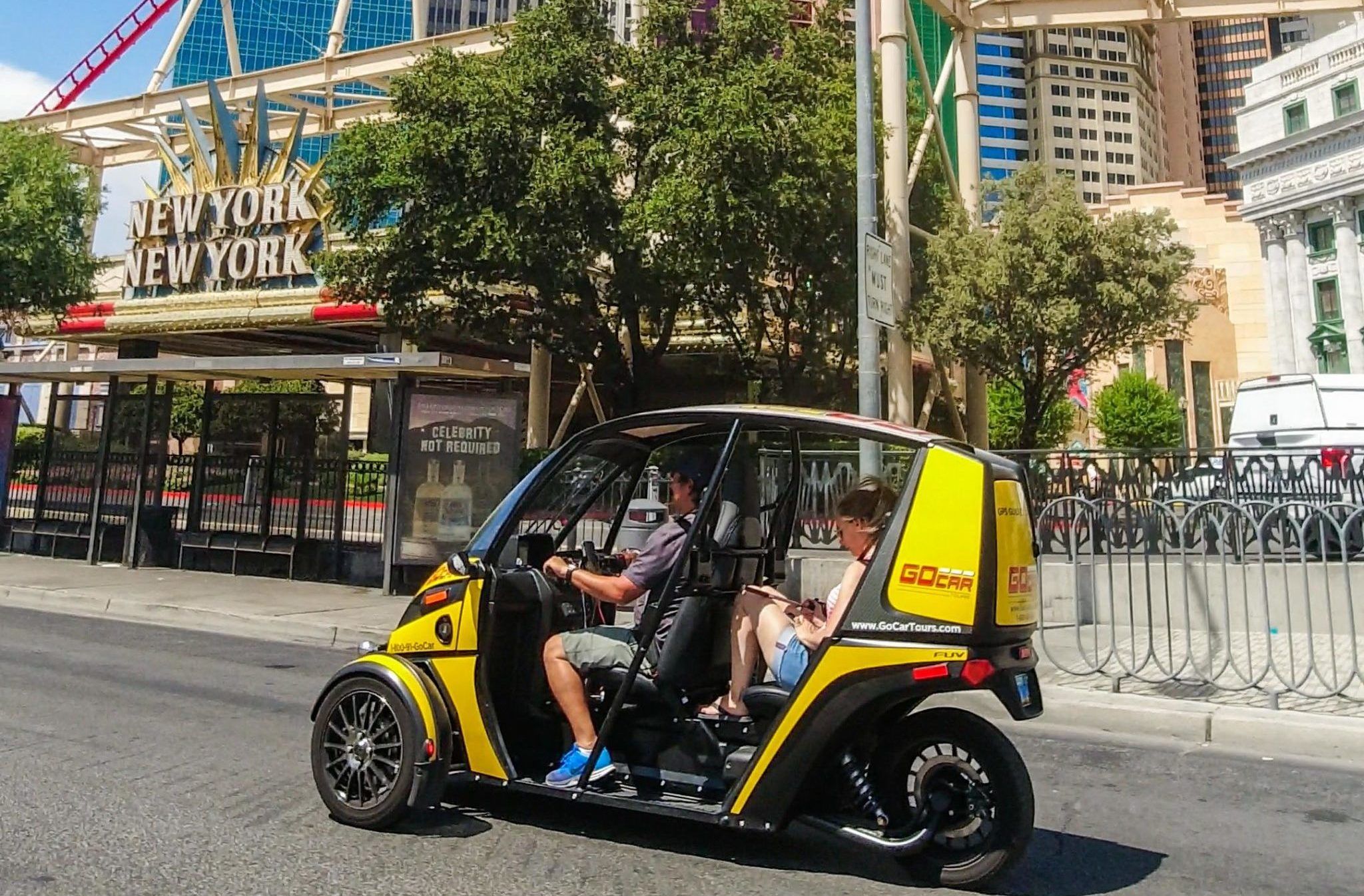 Yellow electric two-seat tour buggy with driver and passenger zipping past a themed hotel facade on the sunny Las Vegas Strip