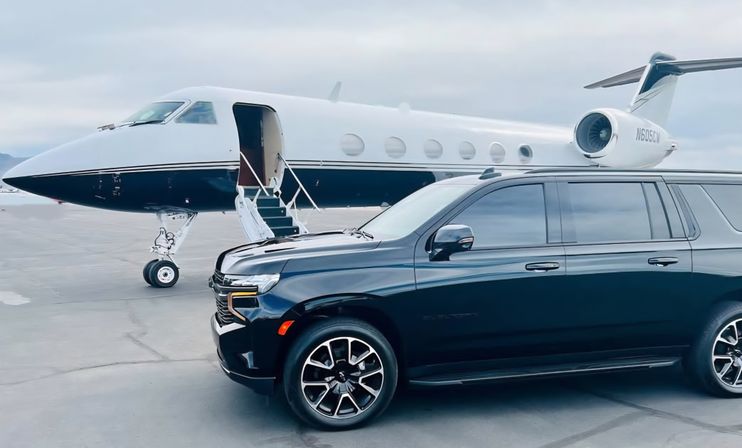 Black luxury SUV parked beside a white private jet with open boarding stairs on an airport tarmac under a cloudy sky