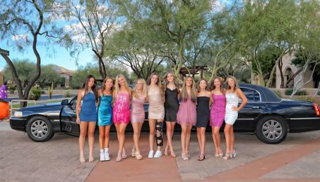 Group of young women in colorful cocktail dresses posing in front of a black stretch limo on a Southwestern desert suburban street with palo verde trees and cacti — pre-prom/formal night.