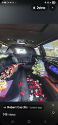 Stretch limousine interior with black leather wraparound seating, scattered red, white and pink rose petals down the aisle, a wrapped bouquet of pink lilies on the side bar, ambient LED lights and a mirrored ceiling—luxury ride ready for a celebration.