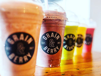 Vibrant fruit smoothies in plastic cups with domed lids lined up on a wooden counter at a juice bar