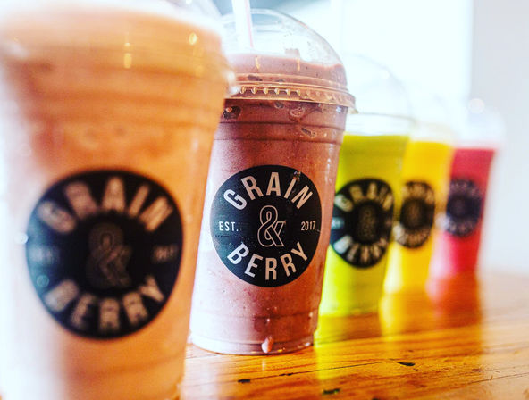 Vibrant fruit smoothies in plastic cups with domed lids lined up on a wooden counter at a juice bar