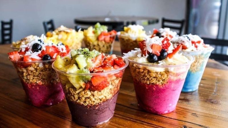 Vibrant acai and smoothie parfait cups layered with granola and topped with sliced strawberries, kiwi, blueberries and shredded coconut on a wooden table in a casual cafe setting