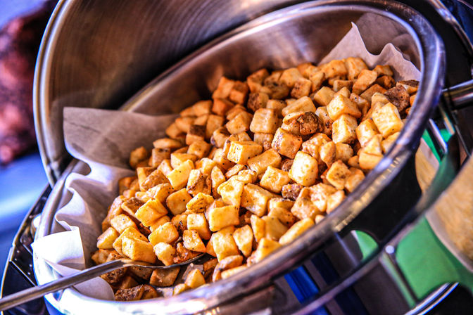 Close-up of golden crispy diced breakfast potatoes (home fries) piled in a stainless-steel buffet chafing dish lined with parchment