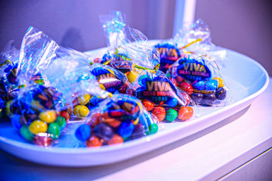 Neon-blue lit party favor bags filled with colorful chocolate candies tied in clear cellophane and arranged on a white platter