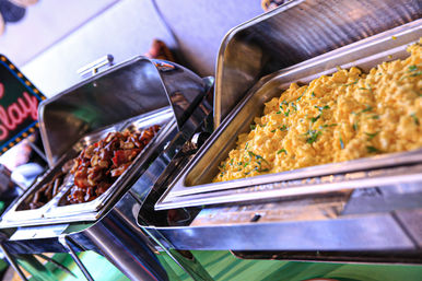 Breakfast buffet station with fluffy scrambled eggs garnished with herbs and crispy bacon served in stainless steel chafing trays