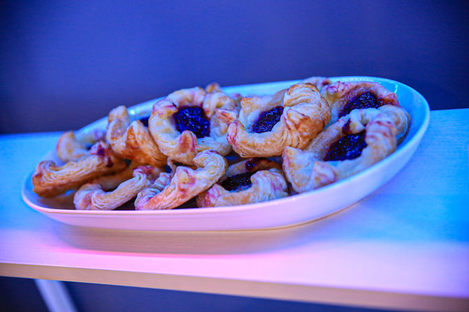 Close-up of flaky jam-filled puff pastries piled on a white plate on a table, bathed in blue-purple ambient lighting.