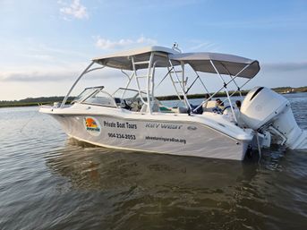 White private tour boat with canopy and outboard engine, passengers relaxing under shade, anchored in a calm coastal marsh at golden hour