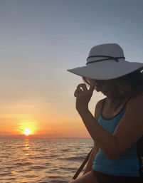 Silhouette of a person in a wide-brimmed sun hat and sunglasses on a boat at a golden ocean sunset