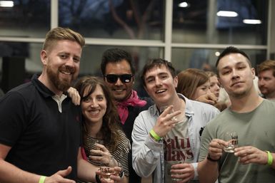 Group of five people smiling and posing at an indoor wine tasting event, holding small glasses marked “Wine Fest” and wearing event wristbands.