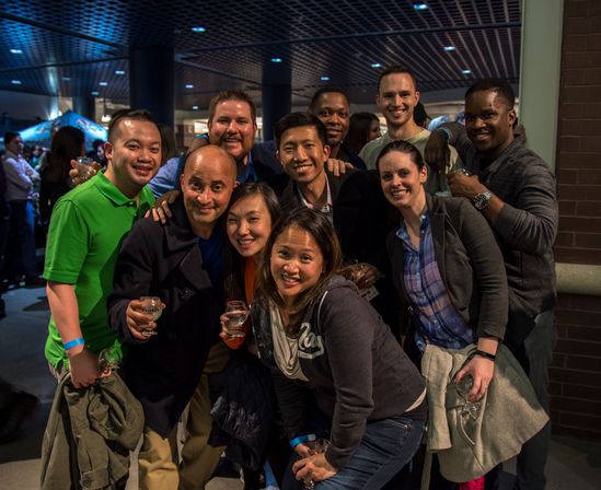 Smiling diverse group posing with drinks at a lively indoor event space, casual attire and wristbands