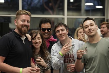 Group of five friends smiling and holding wine glasses at an indoor wine tasting event, casual attire and festive atmosphere
