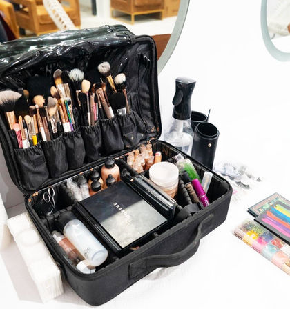 Open black professional makeup case on a white vanity, filled with fluffy brushes, foundation bottles, palettes, colorful eyeshadows, spray bottle and false lashes — ready for glam.