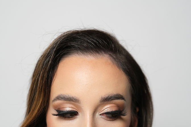 Close-up studio shot of a woman's forehead and eyes with metallic bronze eyeshadow, winged eyeliner and long false lashes — professional makeup beauty look.