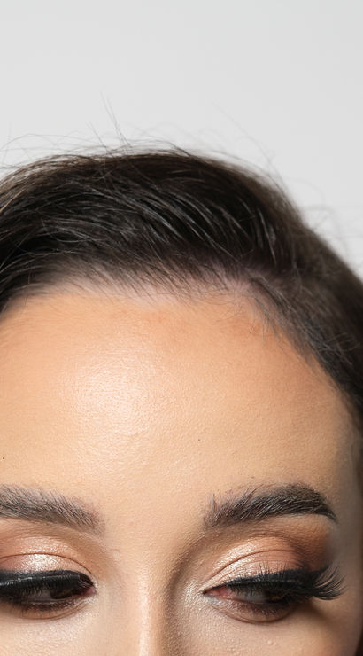 Close-up studio shot of a woman's forehead and eyes with metallic bronze eyeshadow, winged eyeliner and long false lashes — professional makeup beauty look.