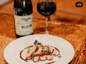 Artfully plated seared duck slices with red wine glaze and microgreens, paired with a glass and bottle of Pinot Noir on a warm wooden table