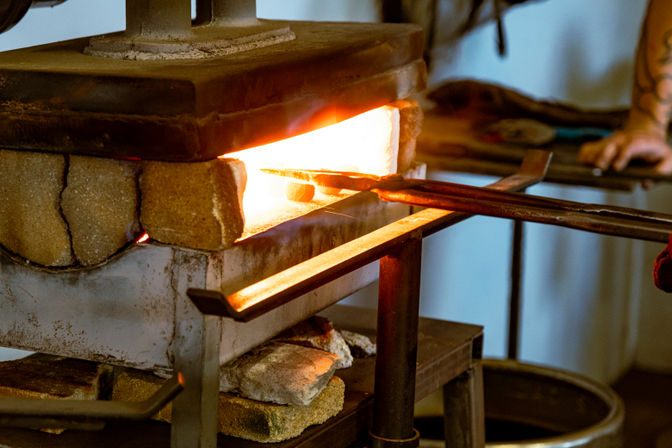 Glowing glassblowing furnace in an artisan studio, molten glass on a metal blowpipe and tongs being heated for shaping