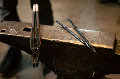 Close-up of a worn blacksmith anvil with a pair of tongs and two metal punches resting on its face in a dim forge workshop.