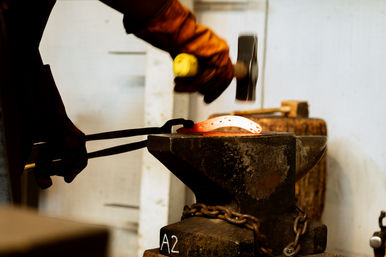 Blacksmith shaping a glowing hot horseshoe on a heavy anvil with tongs and hammer in a metalworking forge workshop