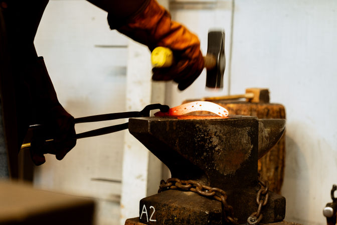 Blacksmith shaping a glowing hot horseshoe on a heavy anvil with tongs and hammer in a metalworking forge workshop