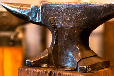 Close-up of a forged knife blade leaning against a weathered iron anvil on a wooden stump in a rustic blacksmith workshop