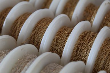 Close-up of white plastic spools holding fine shiny gold metallic chain trim, textured loops on multiple reels for jewelry-making and craft supplies
