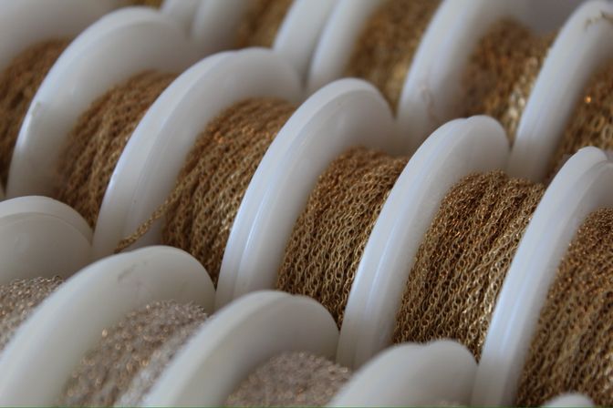 Close-up of white plastic spools holding fine shiny gold metallic chain trim, textured loops on multiple reels for jewelry-making and craft supplies