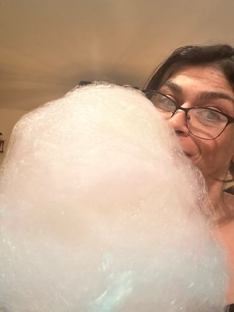 Close-up indoor selfie of a person wearing glasses enjoying a giant fluffy pink-white cotton candy