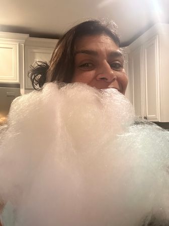 Smiling person peeking over a giant fluffy pink-white cotton candy cloud in a home kitchen with white cabinets