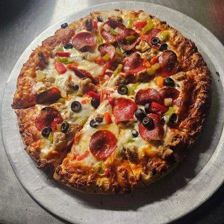 Oven-baked pepperoni pizza sliced and mouthwatering, topped with melted mozzarella, black olives, green and red peppers and sausage on a crispy golden crust, served on a round metal pizza pan.