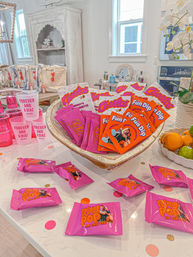 Bright home kitchen island styled for a pink-themed bachelorette party with a bowl of individually wrapped Cheetos and Fun Dip, scattered pink Ring Pop favor packs reading “She Said Yes,” pink party cups, and a bowl of citrus.