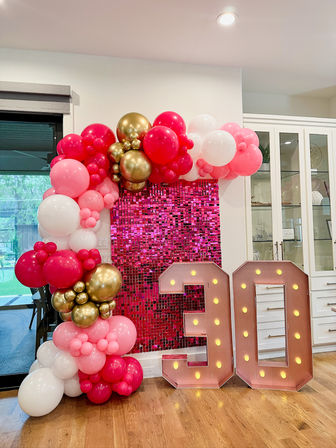 Indoor kitchen party backdrop with pink sequin wall, pink-white-gold balloon arch and illuminated 30 marquee numbers on hardwood floor