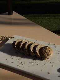 Sliced multigrain seeded loaf fanned on a white marble board on an outdoor patio table, seeds scattered around, warm sunlight and grassy background.