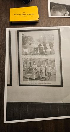Yellow bakery business card on a dark wood table beside a large black-and-white vintage photo print framed on paper