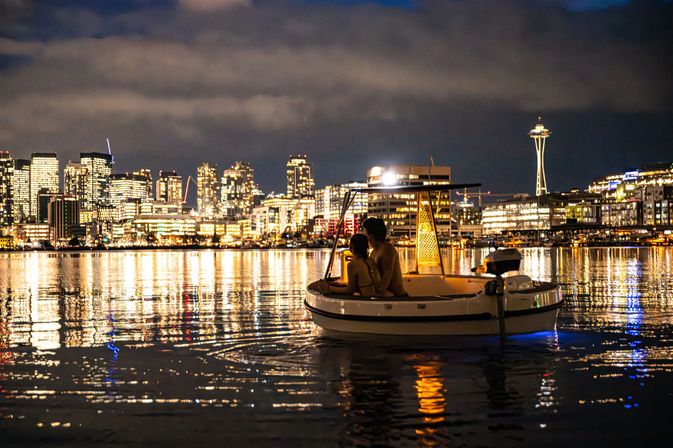 Couple on a cozy illuminated boat at night on calm water with the Seattle skyline and Space Needle glowing in the background, city lights sparkling and reflecting on the rippled water.