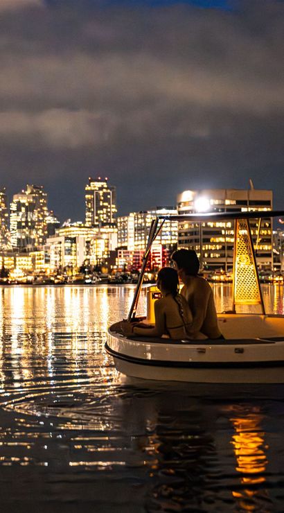 Couple on a cozy illuminated boat at night on calm water with the Seattle skyline and Space Needle glowing in the background, city lights sparkling and reflecting on the rippled water.