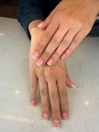 Close-up of hands with a chic pink French manicure - short rounded nails with crisp white tips resting on a light marble countertop.