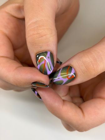 Close-up of fingers with glossy olive-green oval nails featuring playful lavender, red and white abstract swirls — modern nail art manicure.