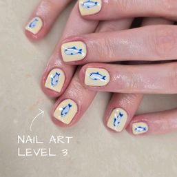 Close-up of glossy short pale-yellow manicure featuring tiny blue fish nail art on each nail — playful, beach-inspired design on hands.