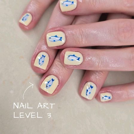 Close-up of glossy short pale-yellow manicure featuring tiny blue fish nail art on each nail — playful, beach-inspired design on hands.