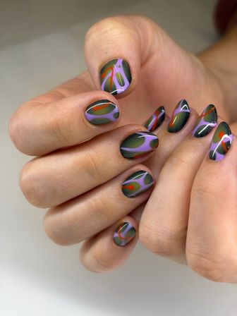 Close-up of hands showing glossy olive-green and lavender abstract swirl nail art manicure with red accents
