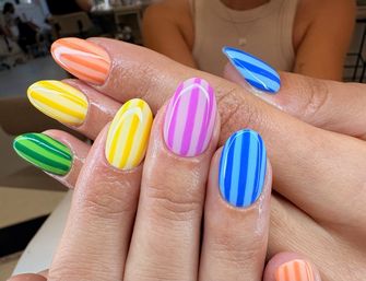 Close-up of glossy almond-shaped nails with bold vertical stripes in rainbow hues (green, yellow, orange, pink, blue) — trendy striped manicure.