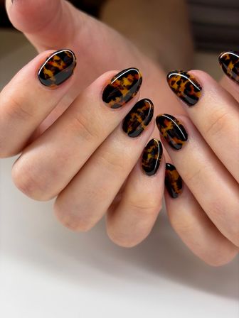 Close-up of glossy almond-shaped tortoiseshell nail art with brown and black marbled spots on natural hands, trendy manicure photo.