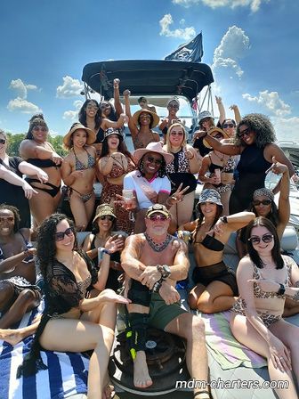 Energetic group of adults in swimsuits posing and cheering on a sunny boat cruise under bright blue skies
