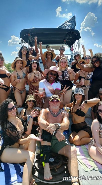 Energetic group of adults in swimsuits posing and cheering on a sunny boat cruise under bright blue skies